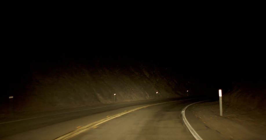 A vehicle is lighting a dark road as it travels