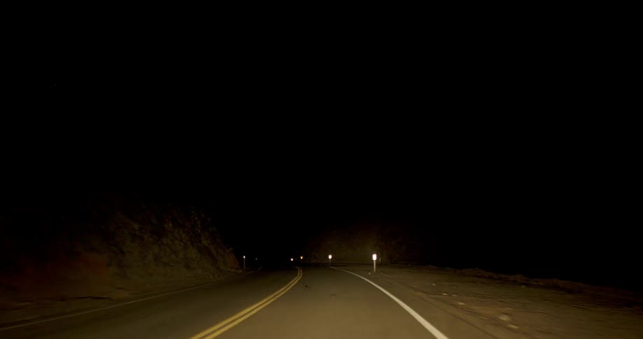 Mile markers reflect light on a two lane road at night