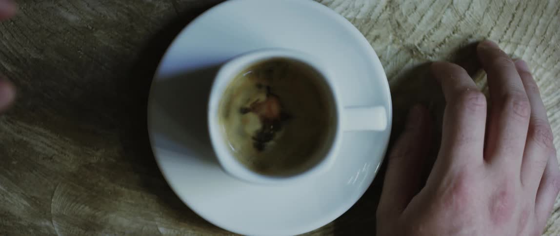A hand drops a sugar cube into a cup of coffee
