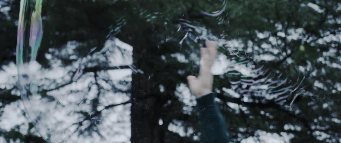 Person swings hand upward to burst large soap bubble blown in the air outdoors