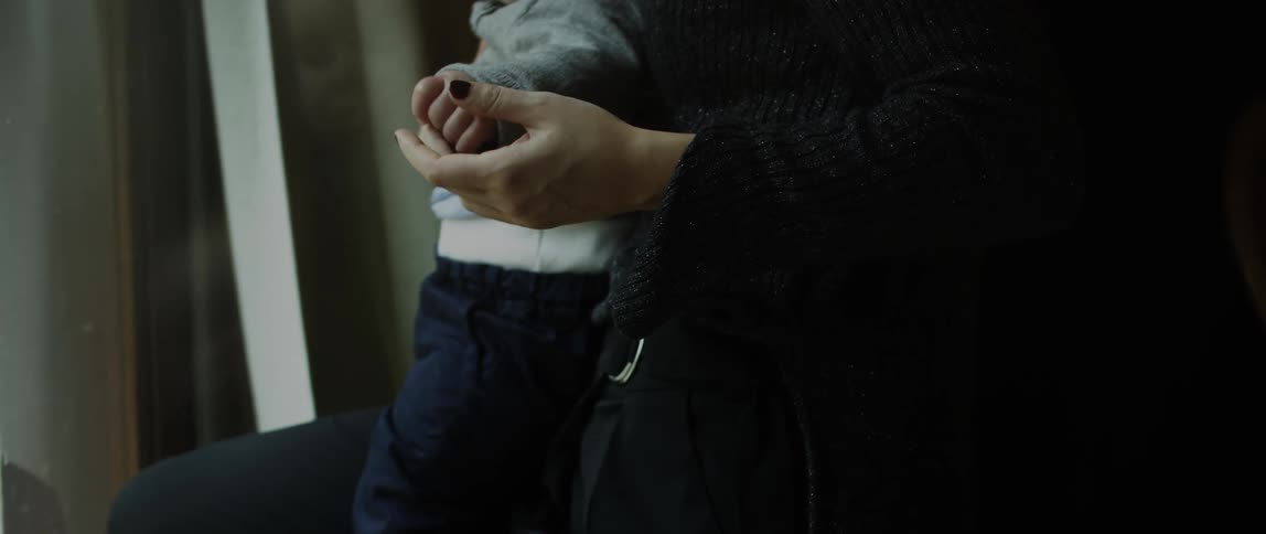 A woman holding up a babys hand as she keeps the baby standing up by holding him close