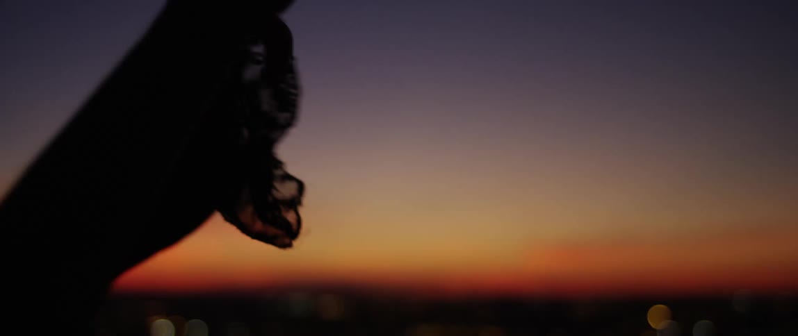 Silhouette of a persons hands and arms dancing overlooking an orange dawn sky