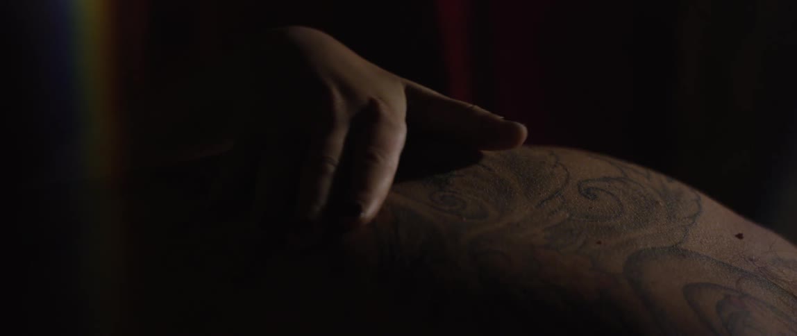 A human hand massaging the back of a person with a tattoo
