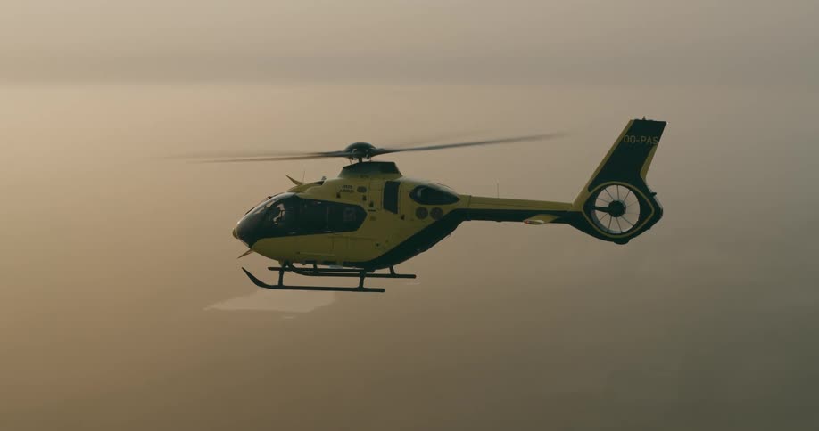A yellow helicopter flying in the sky at sunset