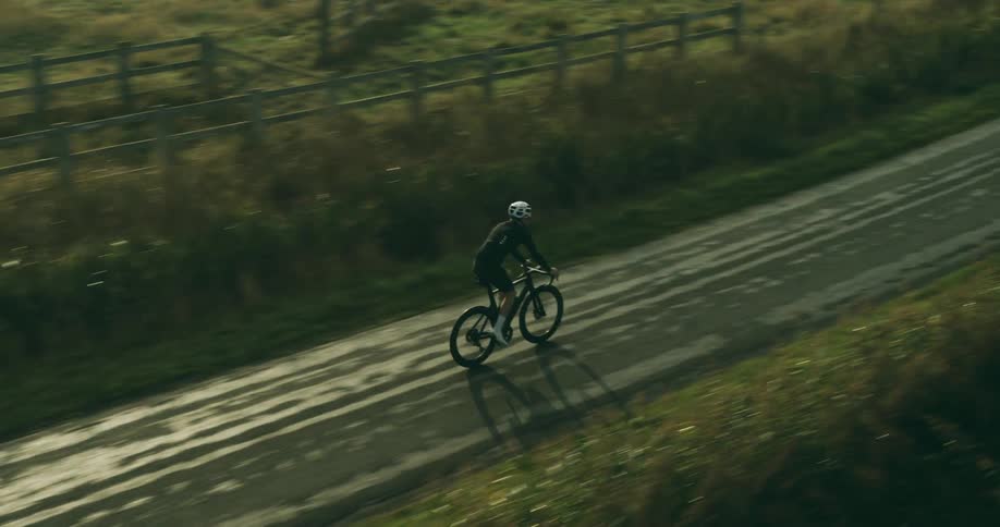 Man cycling on a bike in the morning riding along a narrow street with pastures around