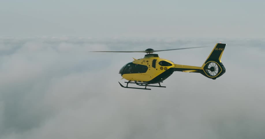 Black and yellow helicopter flies above the clouds