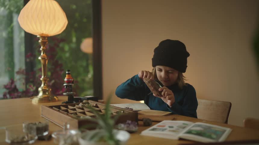 Boy sitting at the table and observing a stone with a magnifying glass