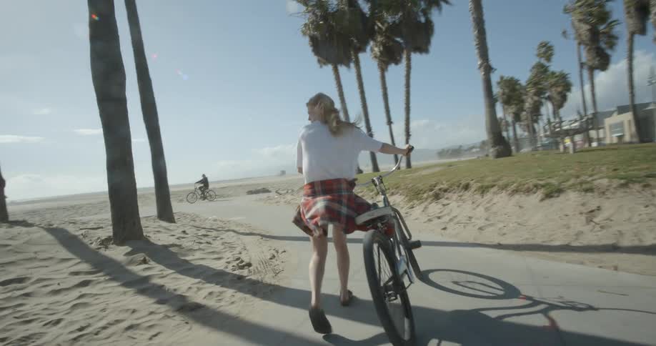 A woman pushes her bike on a path by a windy beach