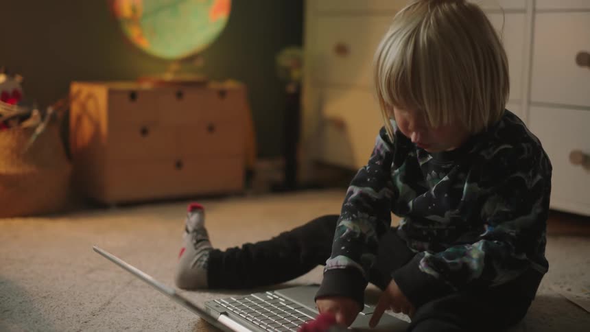 Boy sitting on the carpet pressing the keys of a laptop