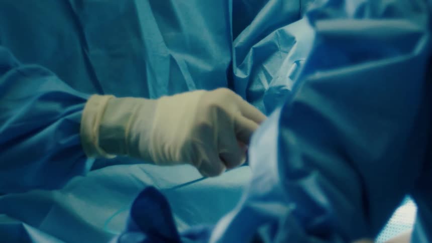Closeup of a surgeons hands in action wearing protective gloves and blue surgical attire