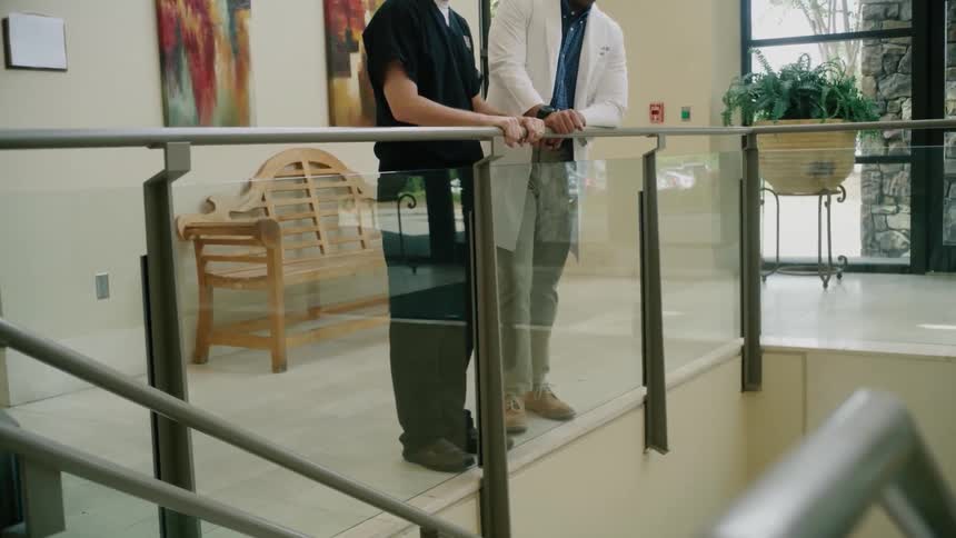Medical professionals stand at rail overlooking staircase and talk