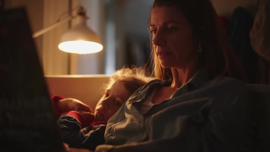 Mother sitting beside her daughter reading a book to her