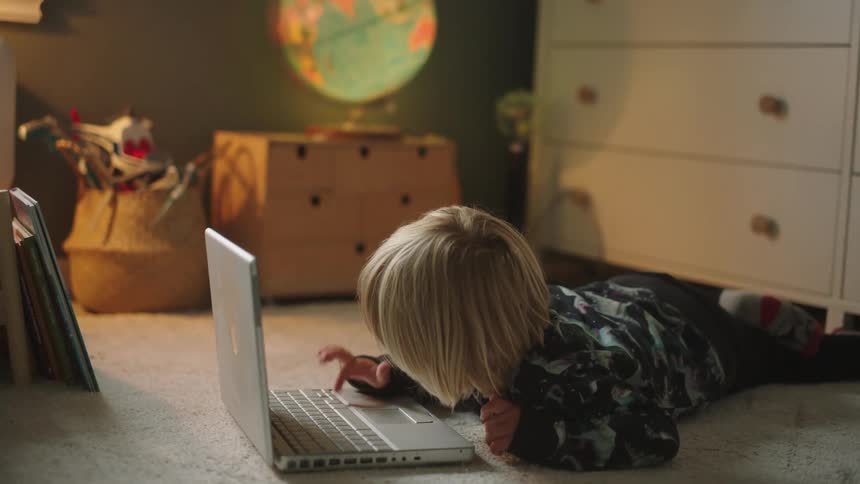 A young boy lying on the floor and playing with a laptop