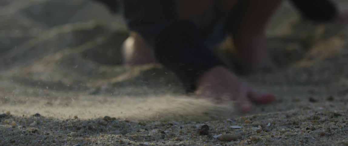 Lady running both hands through the sand at sunset while in a squat position