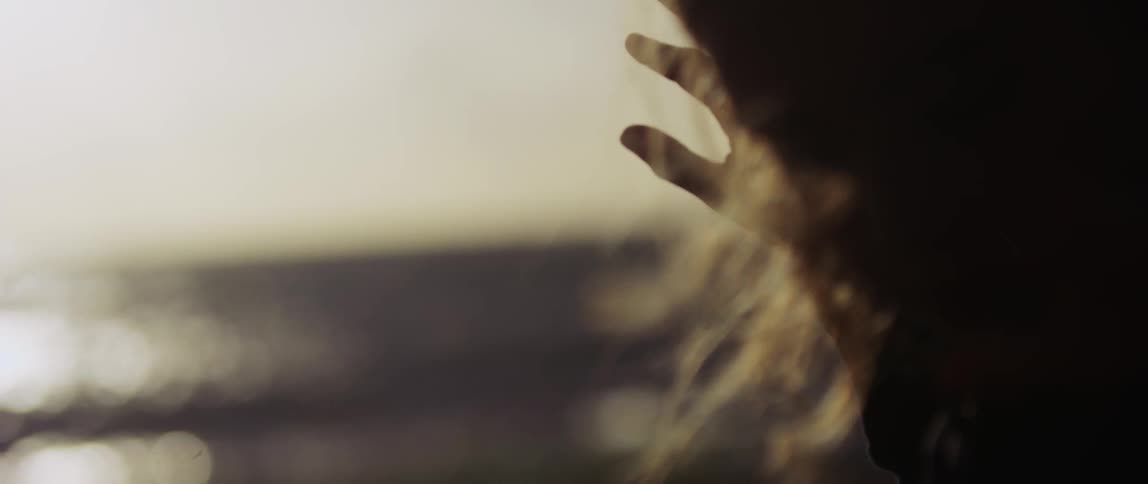 Woman standing on windy beach holds hand up to block the sunlight