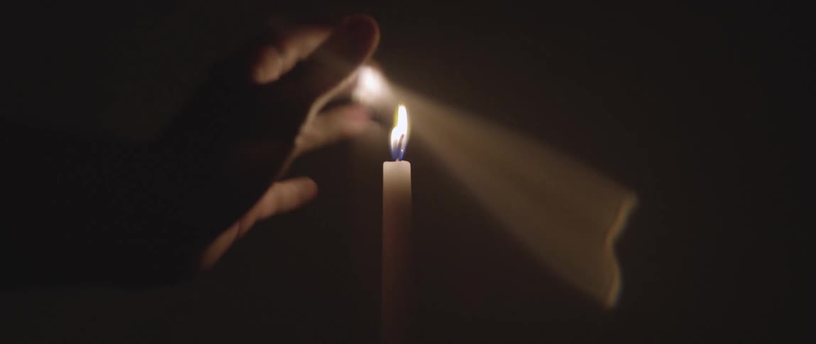 A person puts their hand near the fire on the candle