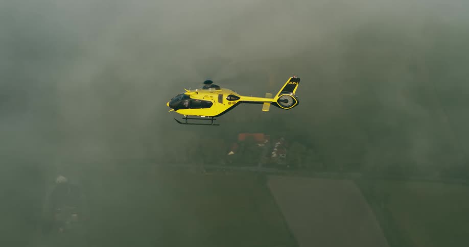 A yellow helicopter flying in a cloudy sky during the day