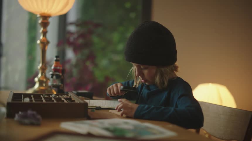 Boy sitting at the table and examining stones with a magnifying glass