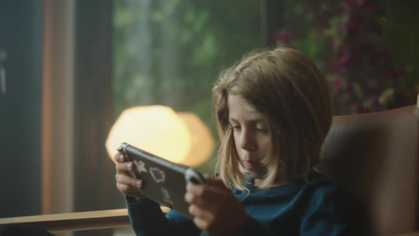 Boy sitting in a chair indoors playing a handheld game with his hands