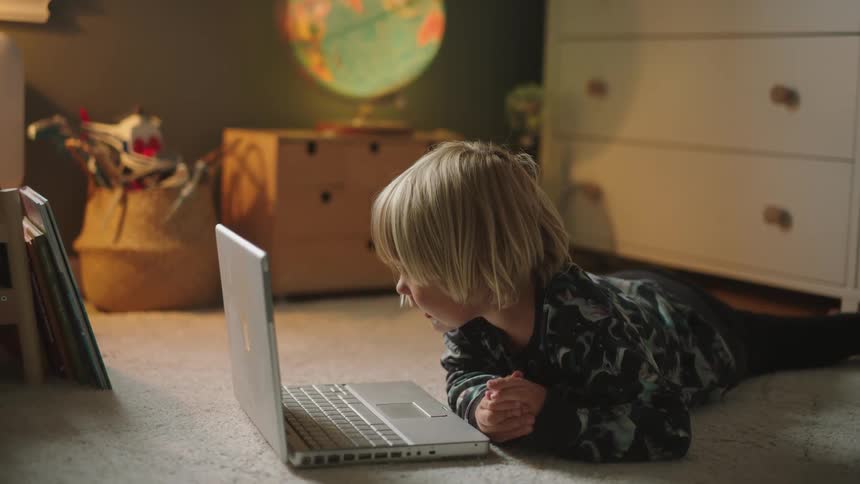 Boy lying on the carpet facing a white laptop
