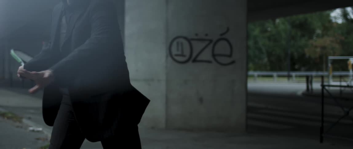 Man in a suit next to an overpass tossing a tennis ball with a racket