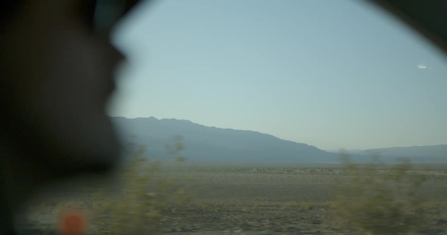 A person is riding in a car passing a vast field