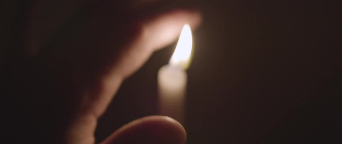 A person gently passing their fingers through the flames of a candle