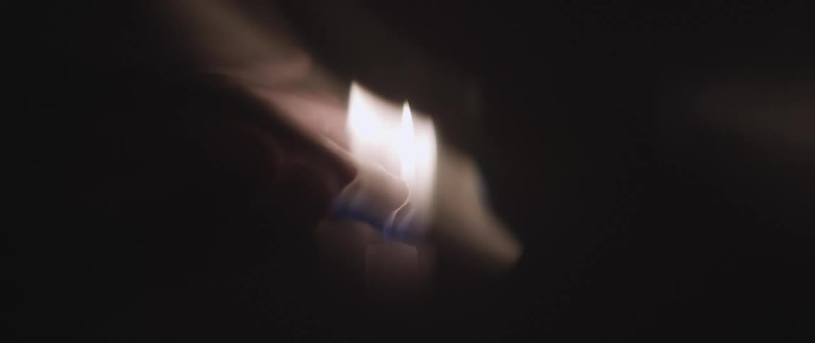 Finger of a person being passed over a lit candle in the dark