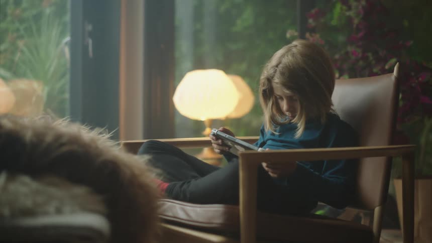 A child playing video game while seated on a chair indoor