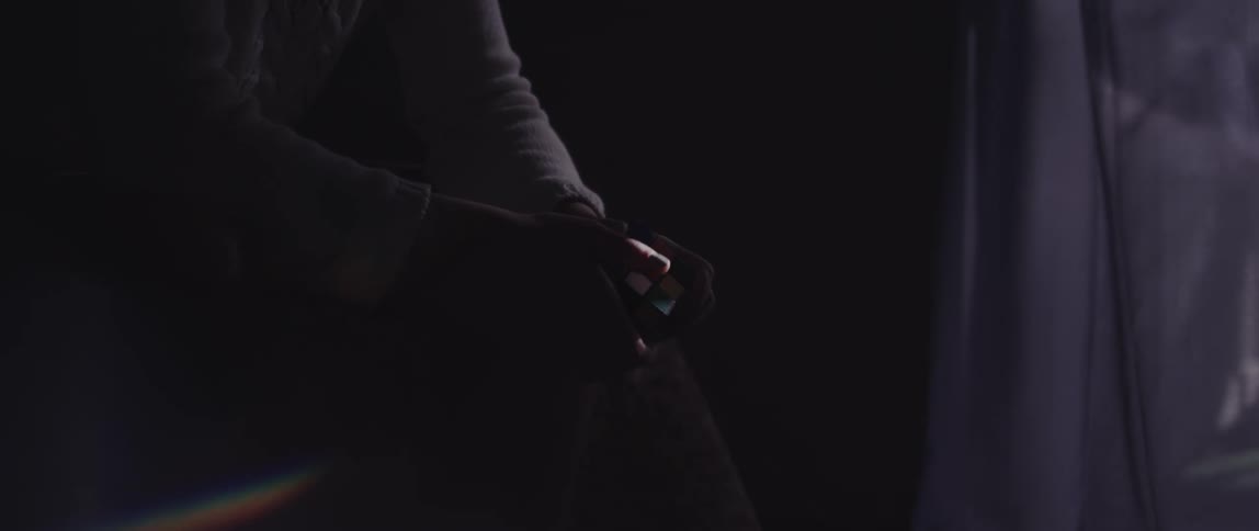 Closeup of a mans hands sitting manipulating a rubiks cube in front of a window with curtains