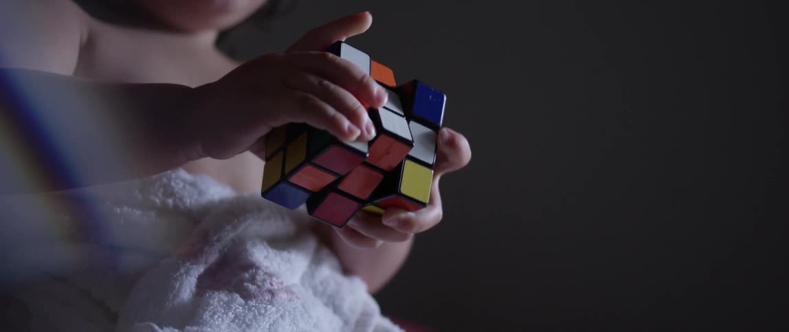 An infant holding a rubiks cube in a dark room