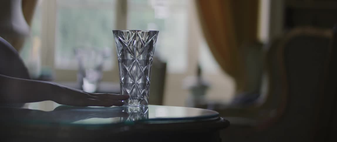Hand of a person pushing a glass vase until it falls