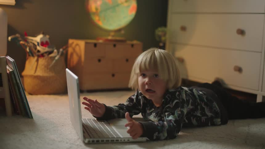 A child typing on the laptop keyboard on the floor