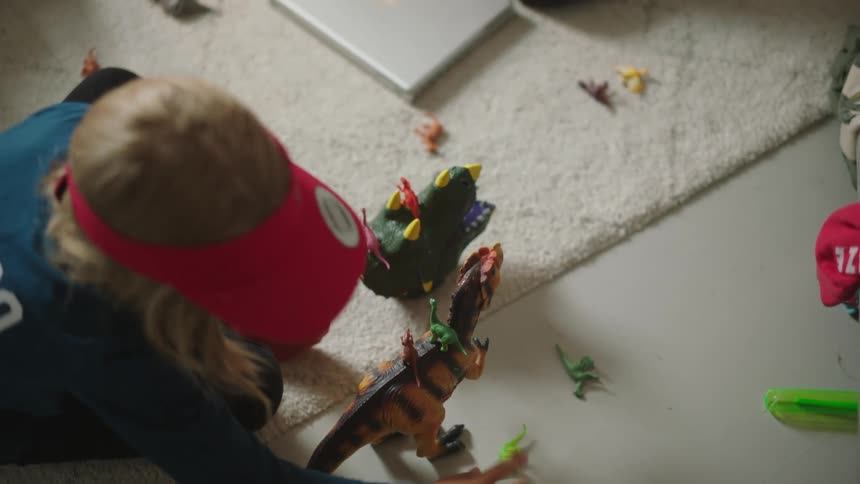 A young boy on the floor playing with dinosaur toys