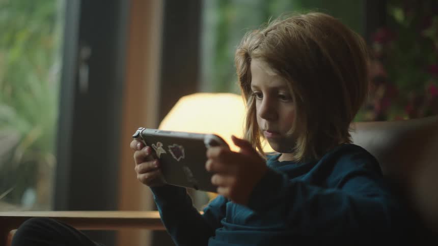 Boy sitting on the couch playing a handheld game with his hands