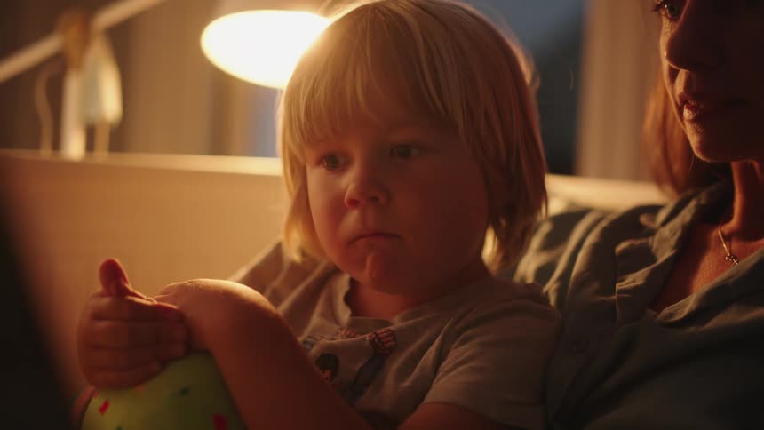 Mother reading to her child while seated on a sofa indoor at night