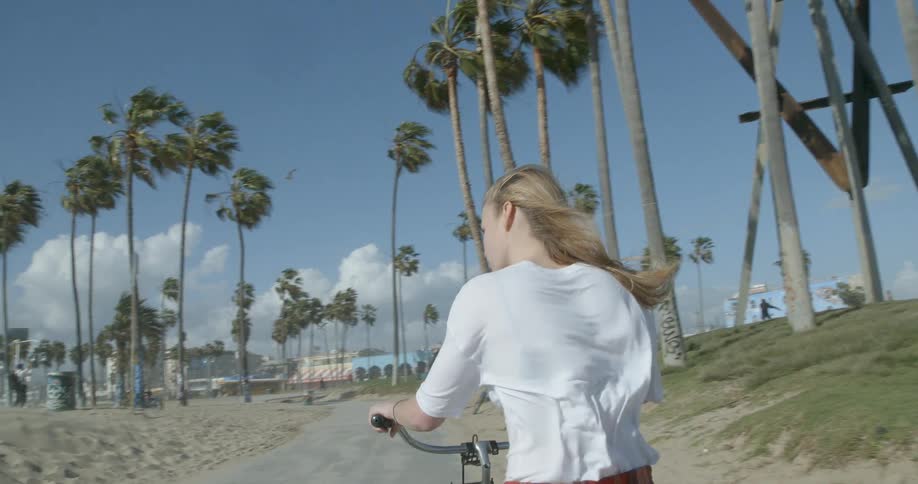 A woman is riding her bike on the beach on a windy day