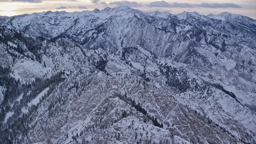 Aerial panorama of peaks and mountains covered in snow under a dawn sky