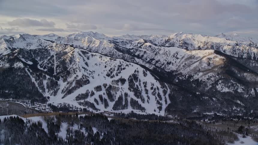 Water fills valley between mountains covered by conifers and snow under a cloudy sky