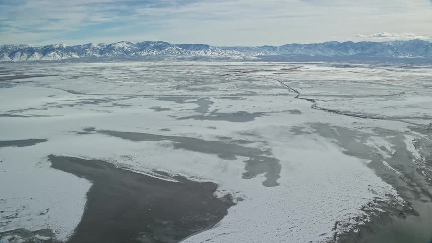 Aerial panorama of snowy plains and lakes with a mountain range on the horizon