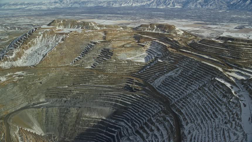 Aerial of brigham canyon mine half in the sun half shadowed lightly dusted with snow with mountains in the background