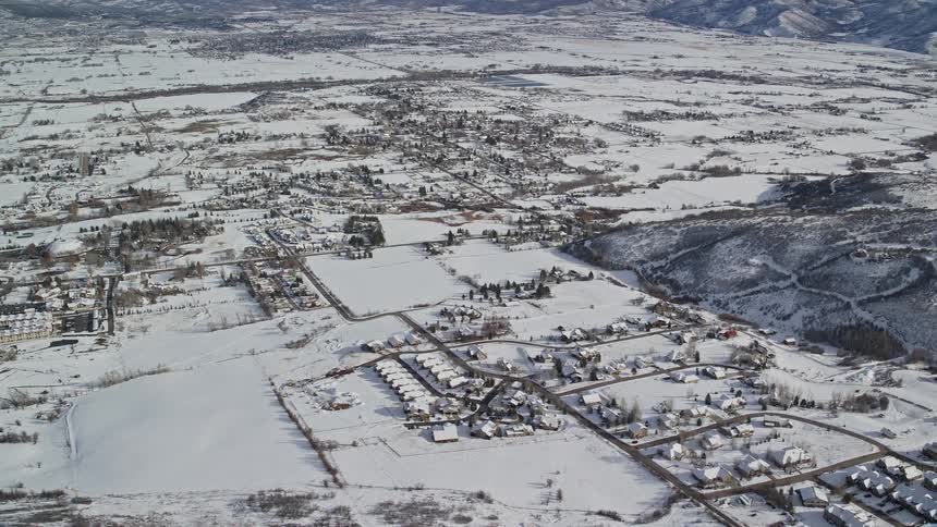 Aerial panorama of an urban city covered in snow amidst hills and beside mountains