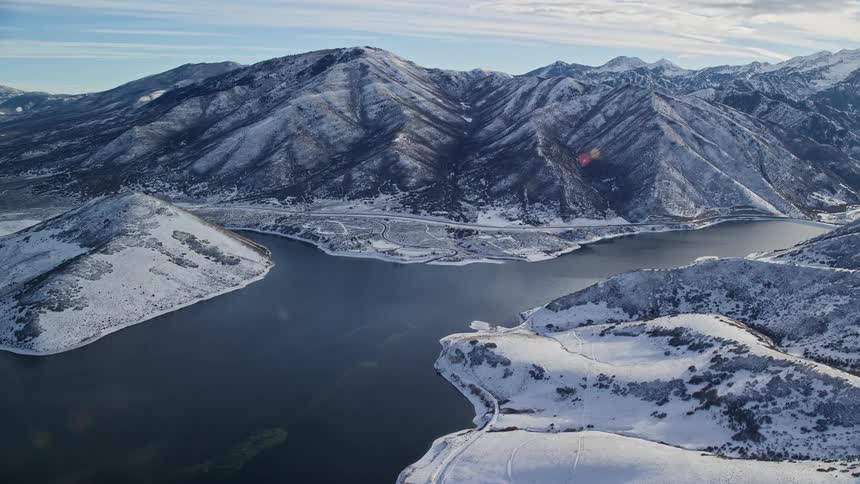 Aerial landscape of a chain of snowcovered mountains facing a lake under a morning sky