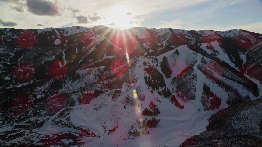 Panoramic view of a mountain range with snowcovered conifers and the morning sun on the horizon