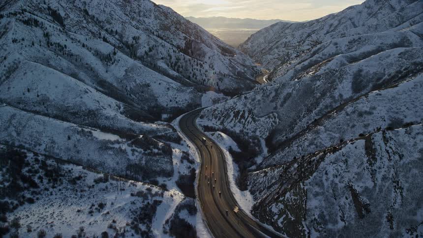 Traffic moves on a mountain valley road between snow covered slopes