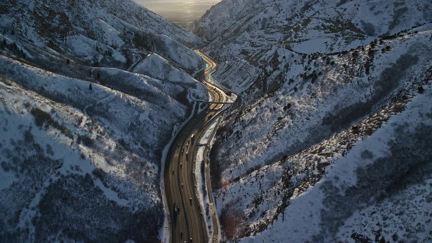 A snow covered mountain range with cars driving on a road between them