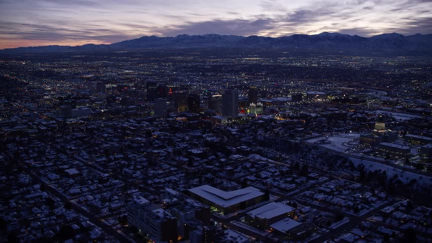 Aerial panoramic of a snow covered salt lake city at dusk with mountains under and an illuminated white sky behind them in the background