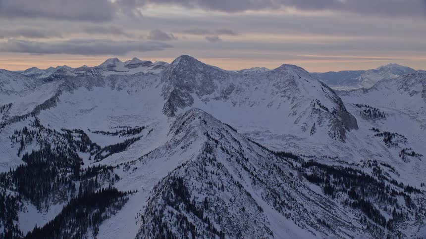 Aerial landscape of a chain of mountains with snowcovered forests and a dawn sky