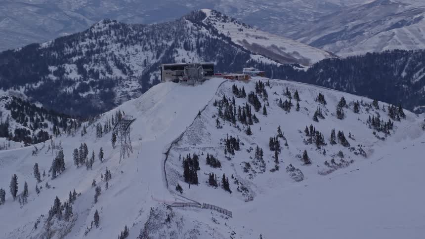 Aerial panorama of power towers on the peak of a snowcovered mountain on a reddish morning sky