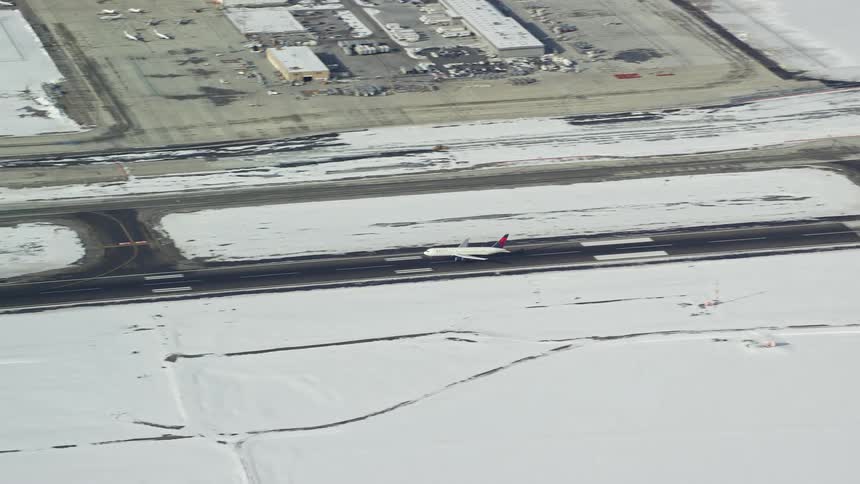 A plane lands on a runway and the weather around is snowy